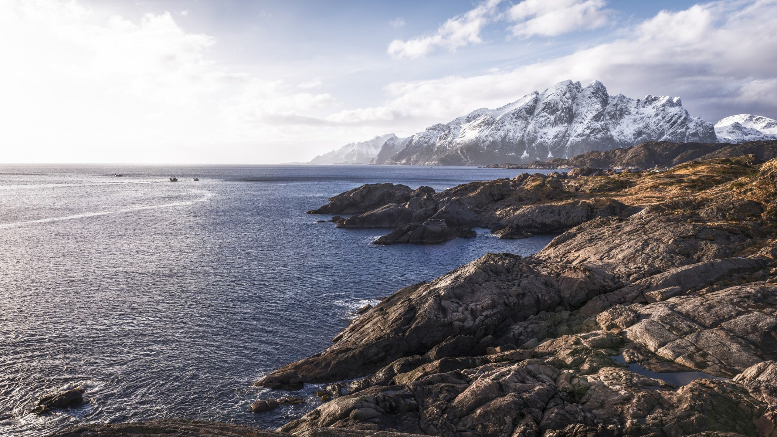 Brown Rocky Mountain Beside Body of Water Under Blue and White Sunny Cloudy Sky During Daytime. Wallpaper in 2560x1440 Resolution