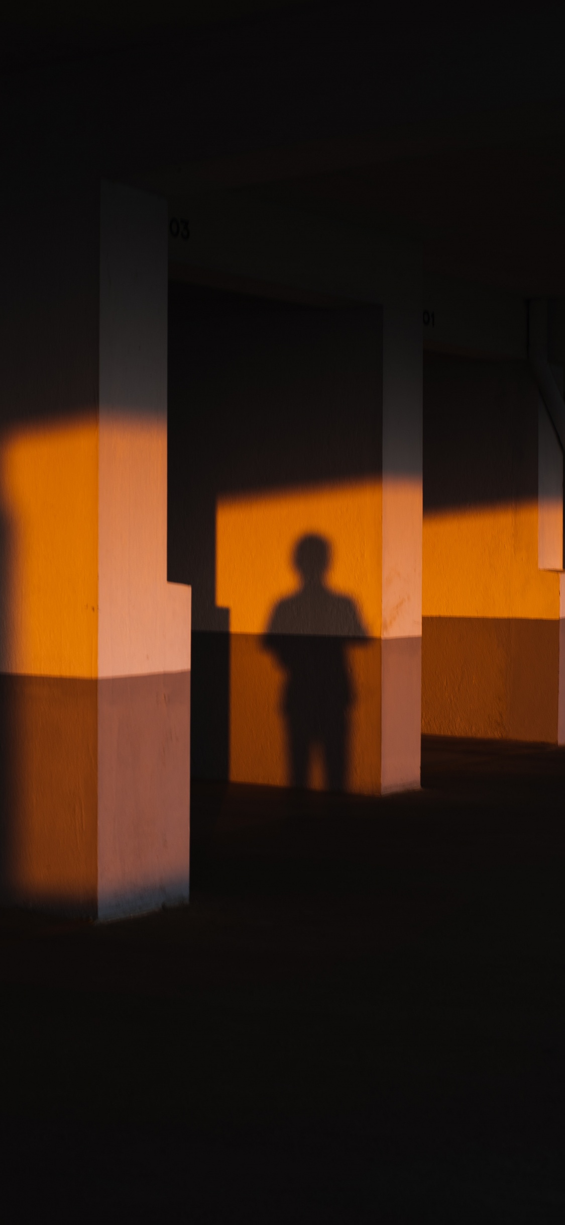 Silhouette Einer Person, Die Vor Einer Braunen Betonwand Steht. Wallpaper in 1125x2436 Resolution