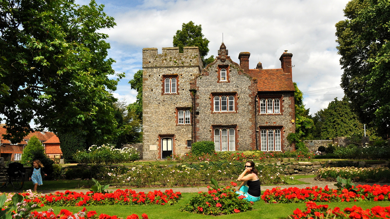 Woman in Black Shirt Sitting on Green Grass Field Near Brown Concrete Building During Daytime. Wallpaper in 1366x768 Resolution