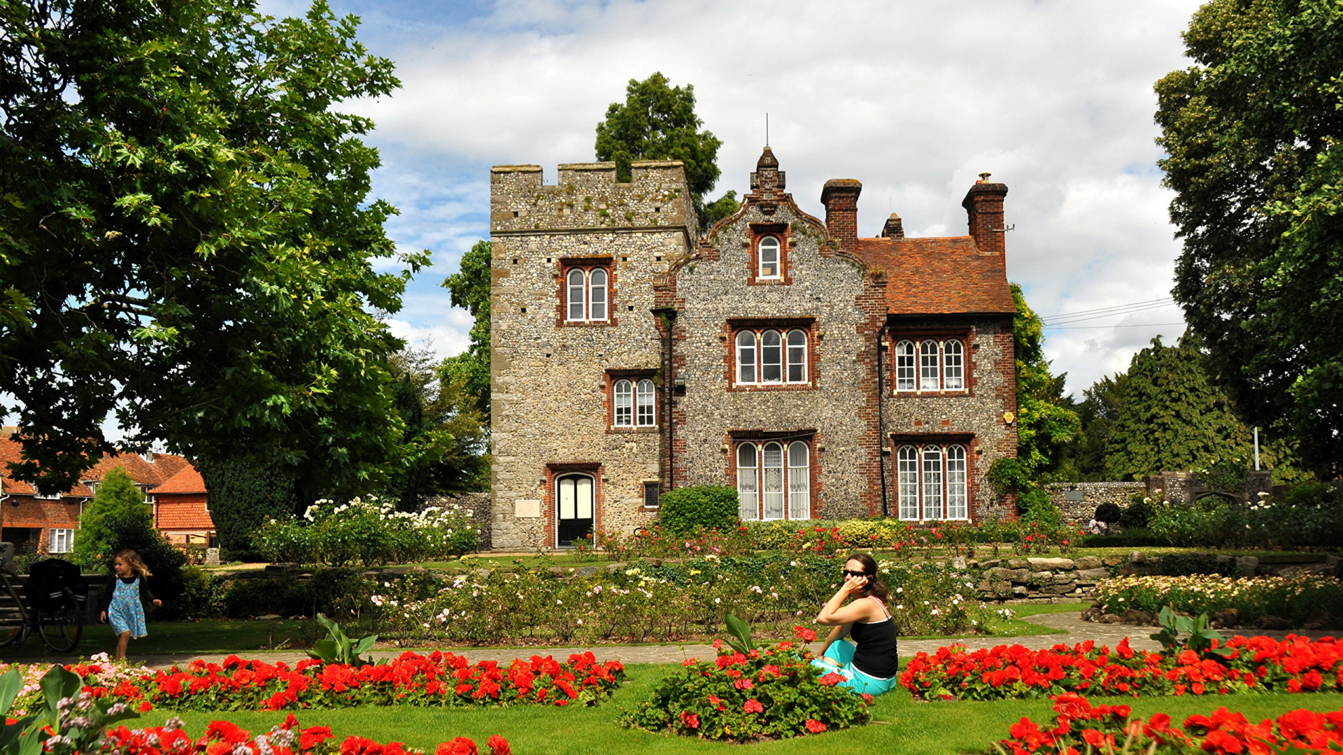 Woman in Black Shirt Sitting on Green Grass Field Near Brown Concrete Building During Daytime. Wallpaper in 1920x1080 Resolution