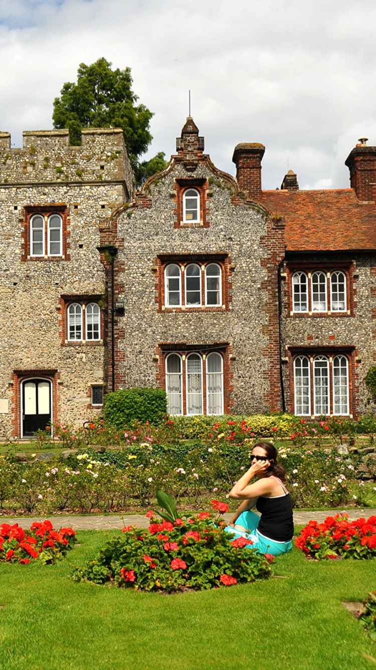 Woman in Black Shirt Sitting on Green Grass Field Near Brown Concrete Building During Daytime. Wallpaper in 750x1334 Resolution