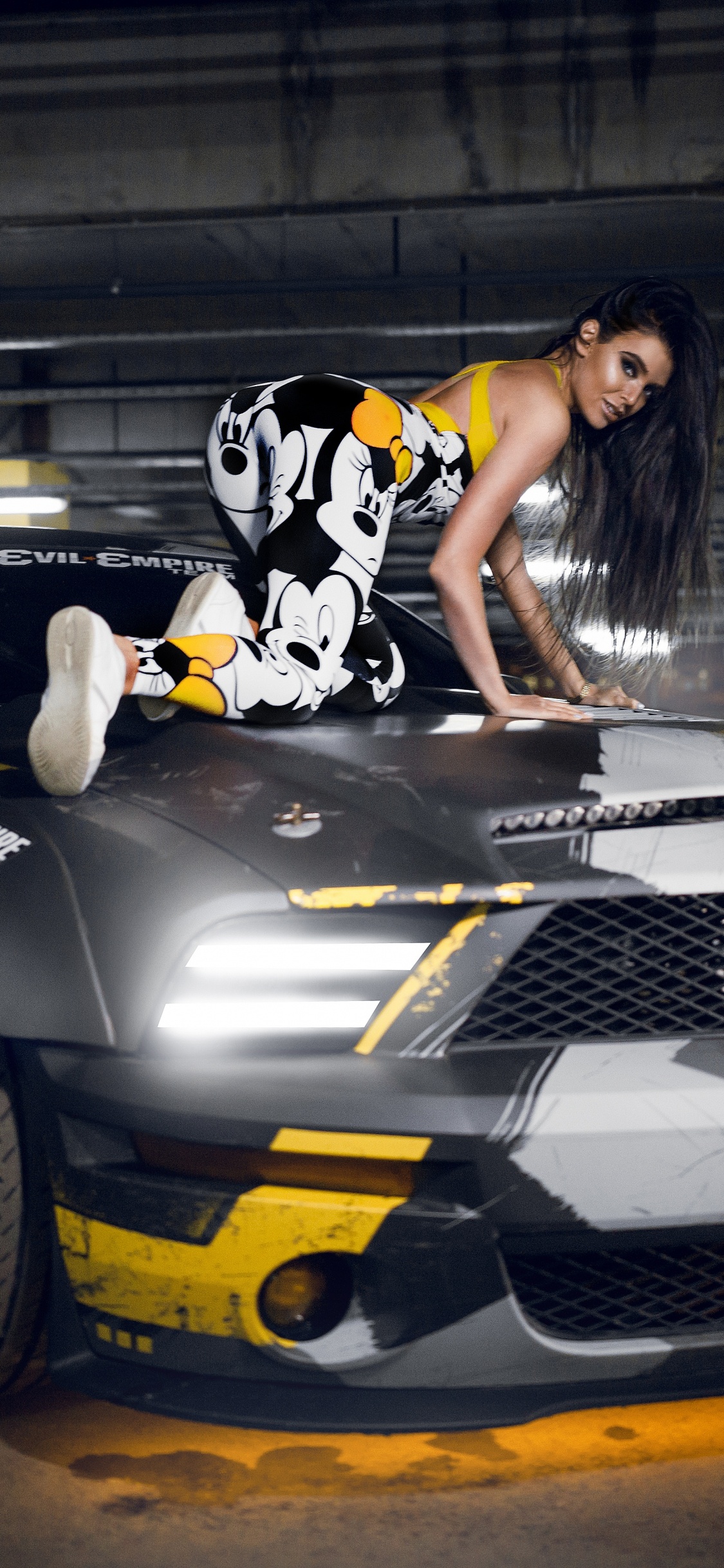 Woman in Black and White Floral Dress Riding on Black and Yellow Sports Car. Wallpaper in 1125x2436 Resolution