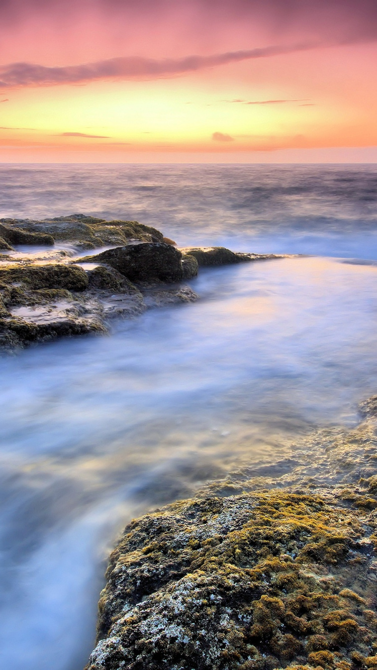 Felsiges Ufer Mit Wasserwellen Bei Sonnenuntergang. Wallpaper in 750x1334 Resolution