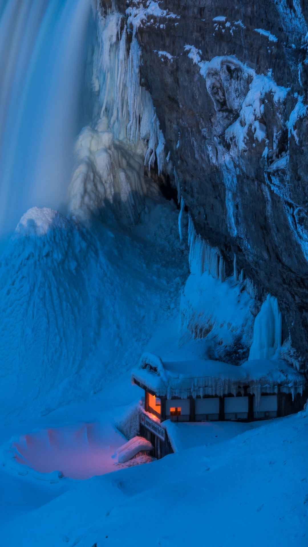 Person in Orange Jacket Sitting on Brown Wooden Dock Near White Snow Covered Mountain During Daytime. Wallpaper in 1080x1920 Resolution