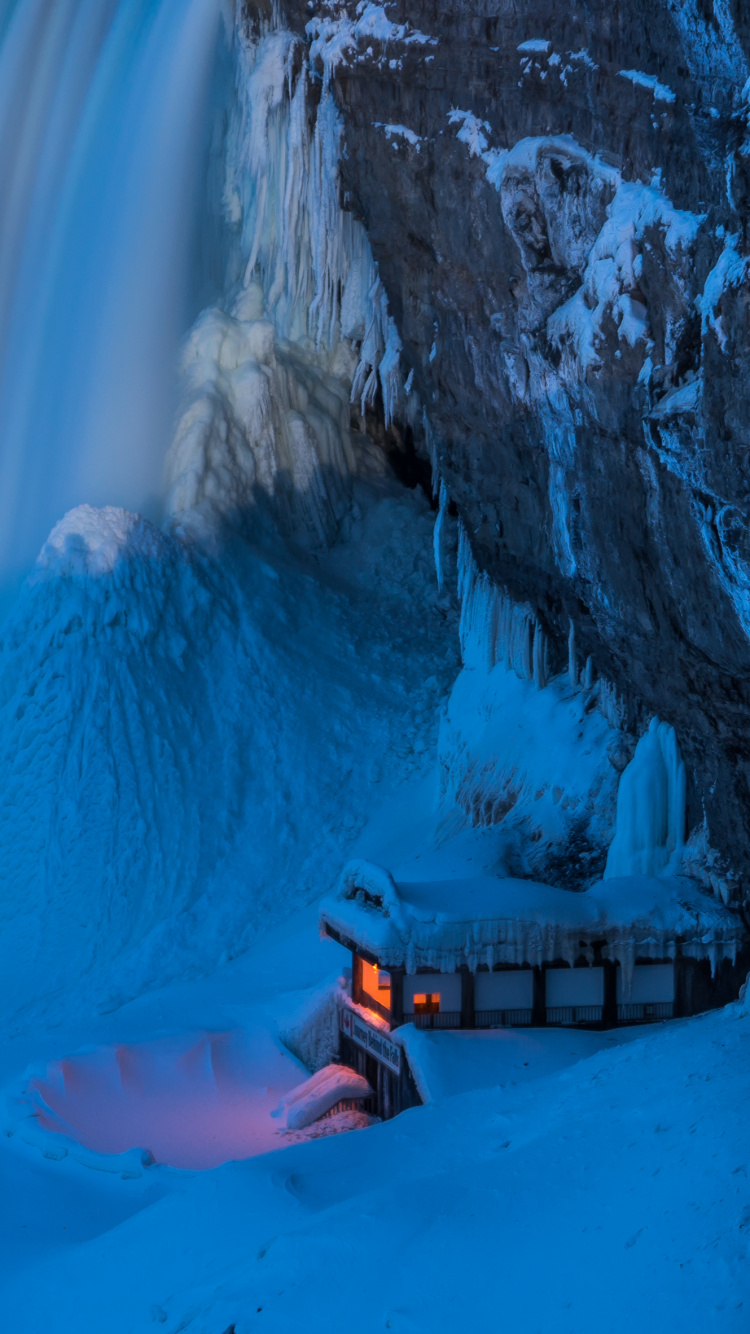 Person in Orange Jacket Sitting on Brown Wooden Dock Near White Snow Covered Mountain During Daytime. Wallpaper in 750x1334 Resolution