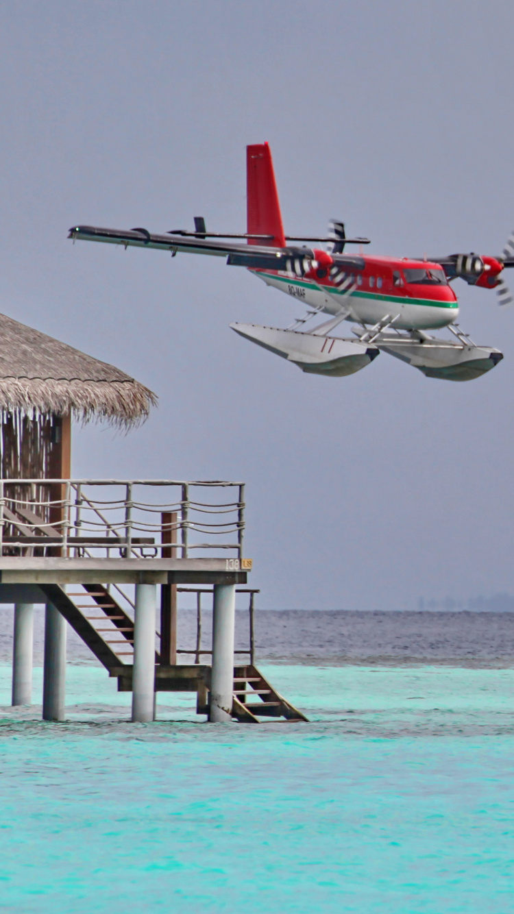 Red and White Plane Flying Over The Sea During Daytime. Wallpaper in 750x1334 Resolution