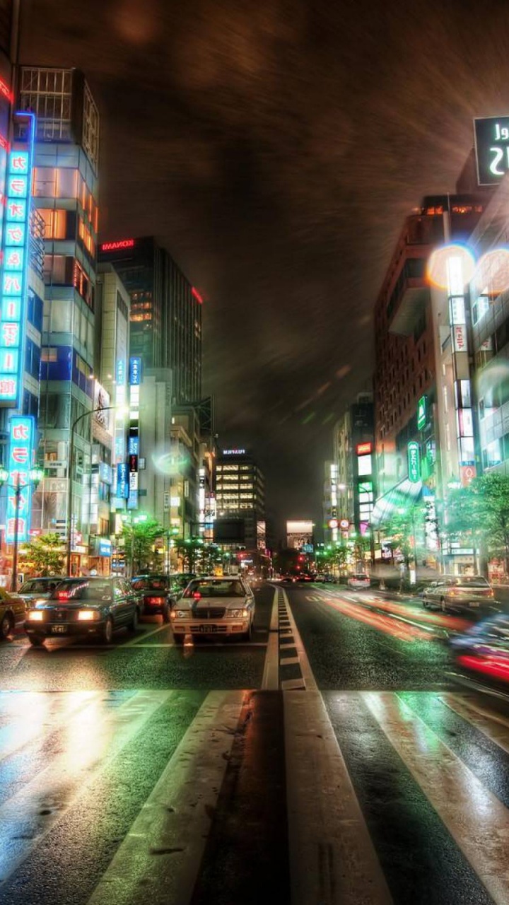 Autos Auf Der Straße Zwischen Hochhäusern Während Der Nacht. Wallpaper in 720x1280 Resolution
