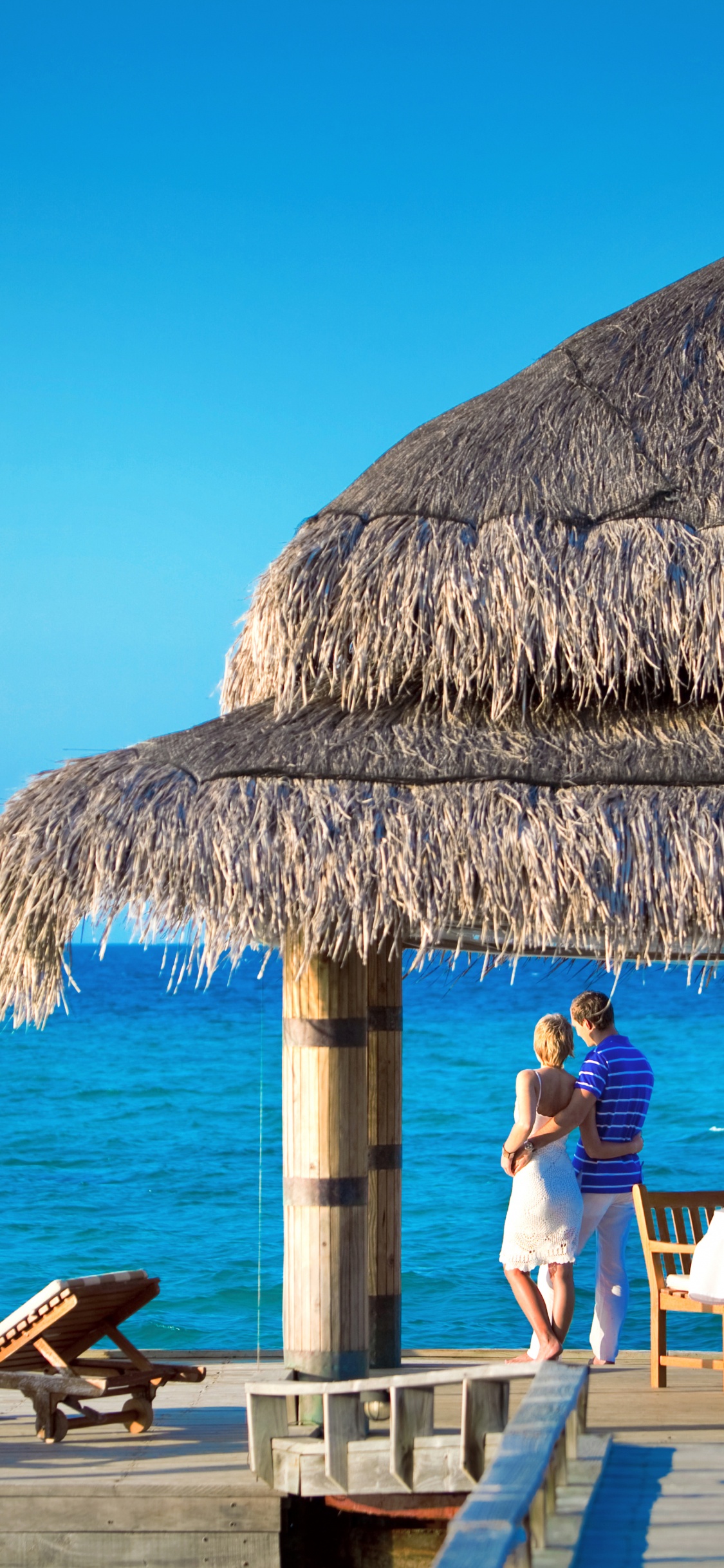 People Sitting on Brown Wooden Chairs Near Brown Nipa Hut During Daytime. Wallpaper in 1125x2436 Resolution