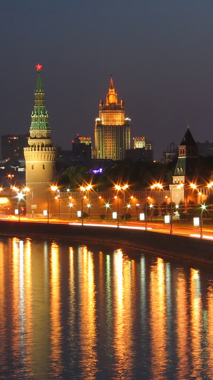 Lighted City Buildings Near Body of Water During Night Time. Wallpaper in 750x1334 Resolution