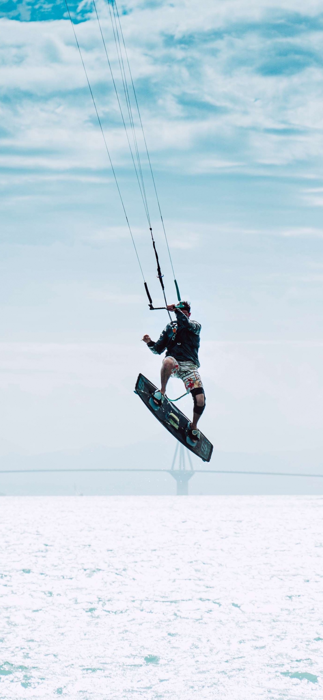 Man in Black Jacket and Black Pants Riding on Black Snowboard Under White Clouds and Blue. Wallpaper in 1125x2436 Resolution