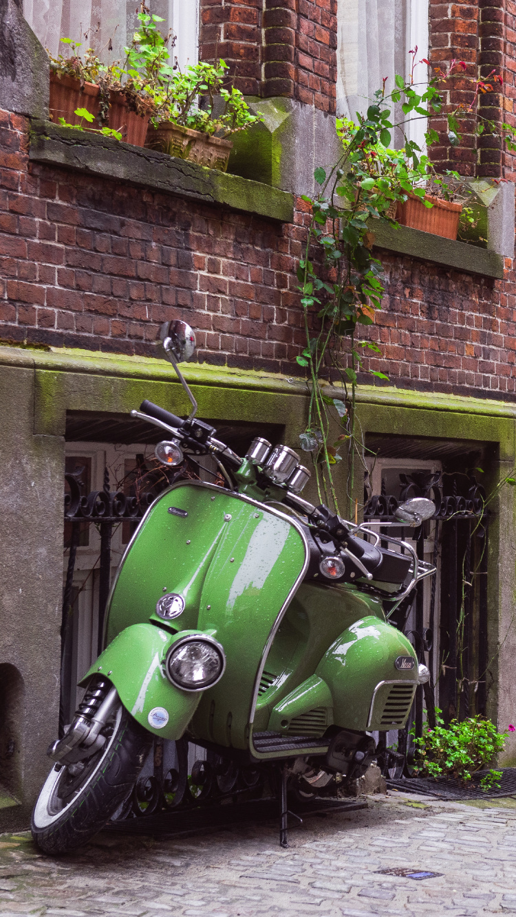 Green Motorcycle Parked Beside Brown Brick Building. Wallpaper in 750x1334 Resolution