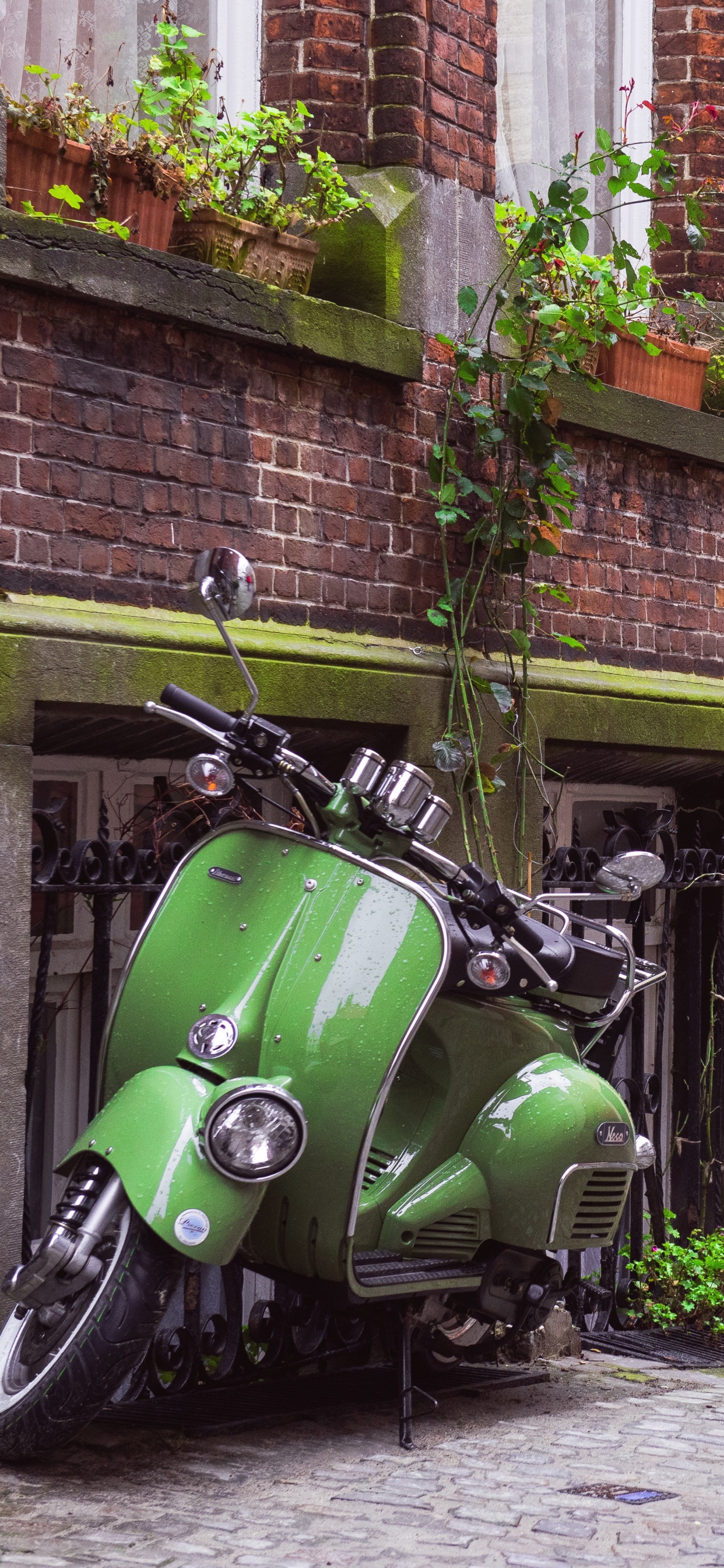 Grünes Motorrad Neben Braunem Backsteingebäude Geparkt. Wallpaper in 1242x2688 Resolution