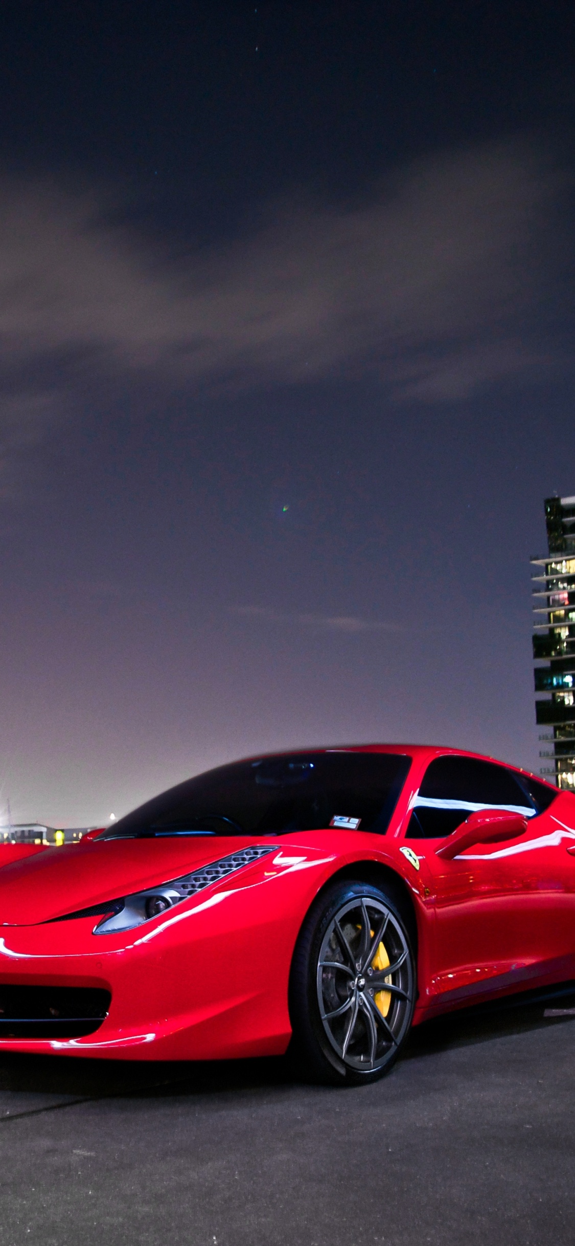 Ferrari Rouge 458 Italia Sur Route Près Des Bâtiments de la Ville Pendant la Nuit. Wallpaper in 1125x2436 Resolution