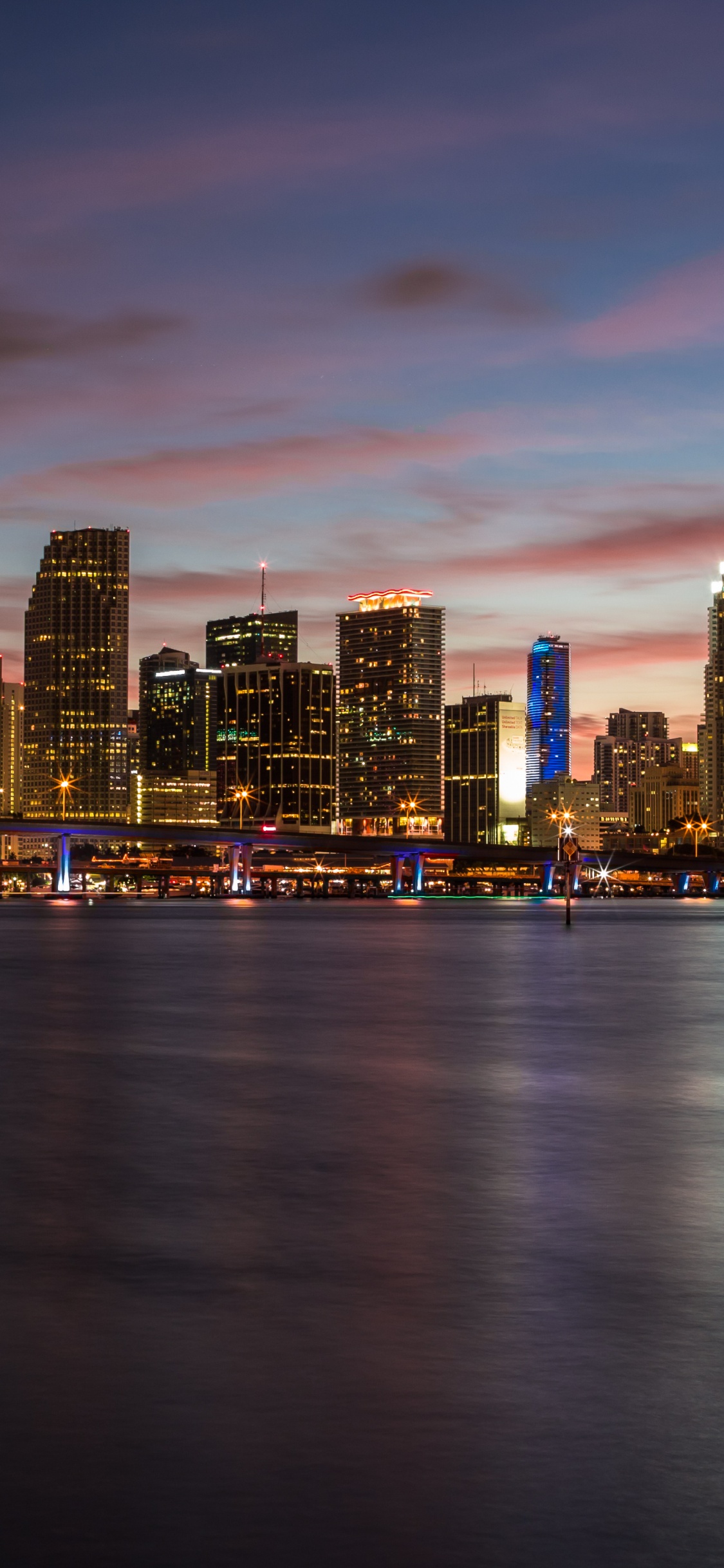 Skyline Der Stadt Über Gewässer Bei Sonnenuntergang. Wallpaper in 1125x2436 Resolution