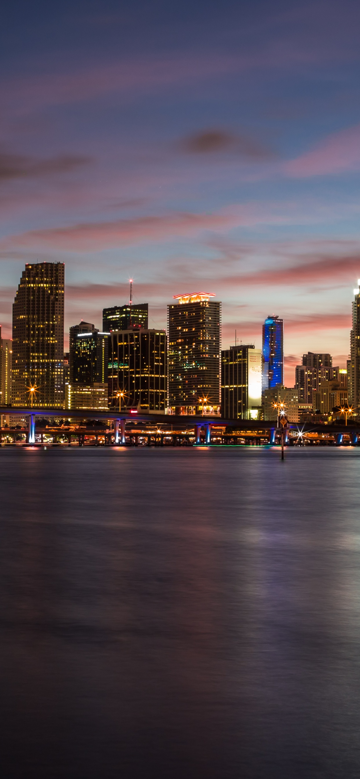 City Skyline Across Body of Water During Sunset. Wallpaper in 1242x2688 Resolution
