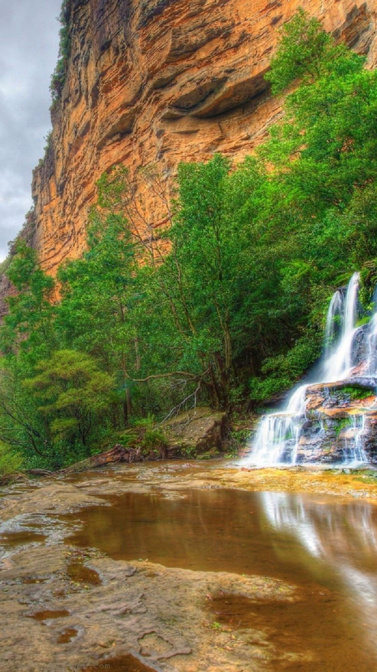 Water Falls Between Brown Rocky Mountain Under Gray Cloudy Sky During Daytime. Wallpaper in 750x1334 Resolution