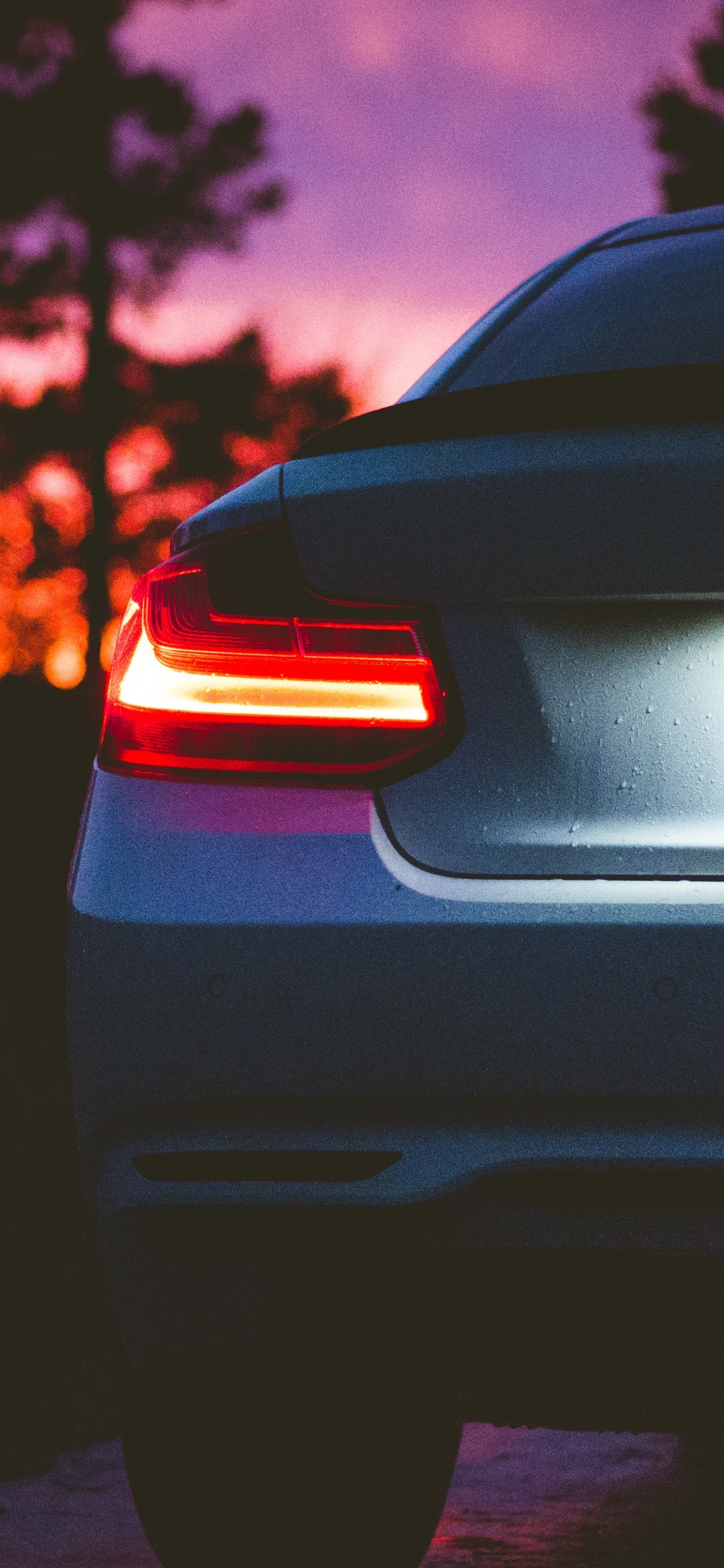 Schwarzes Auto Auf Der Straße Bei Sonnenuntergang. Wallpaper in 1125x2436 Resolution