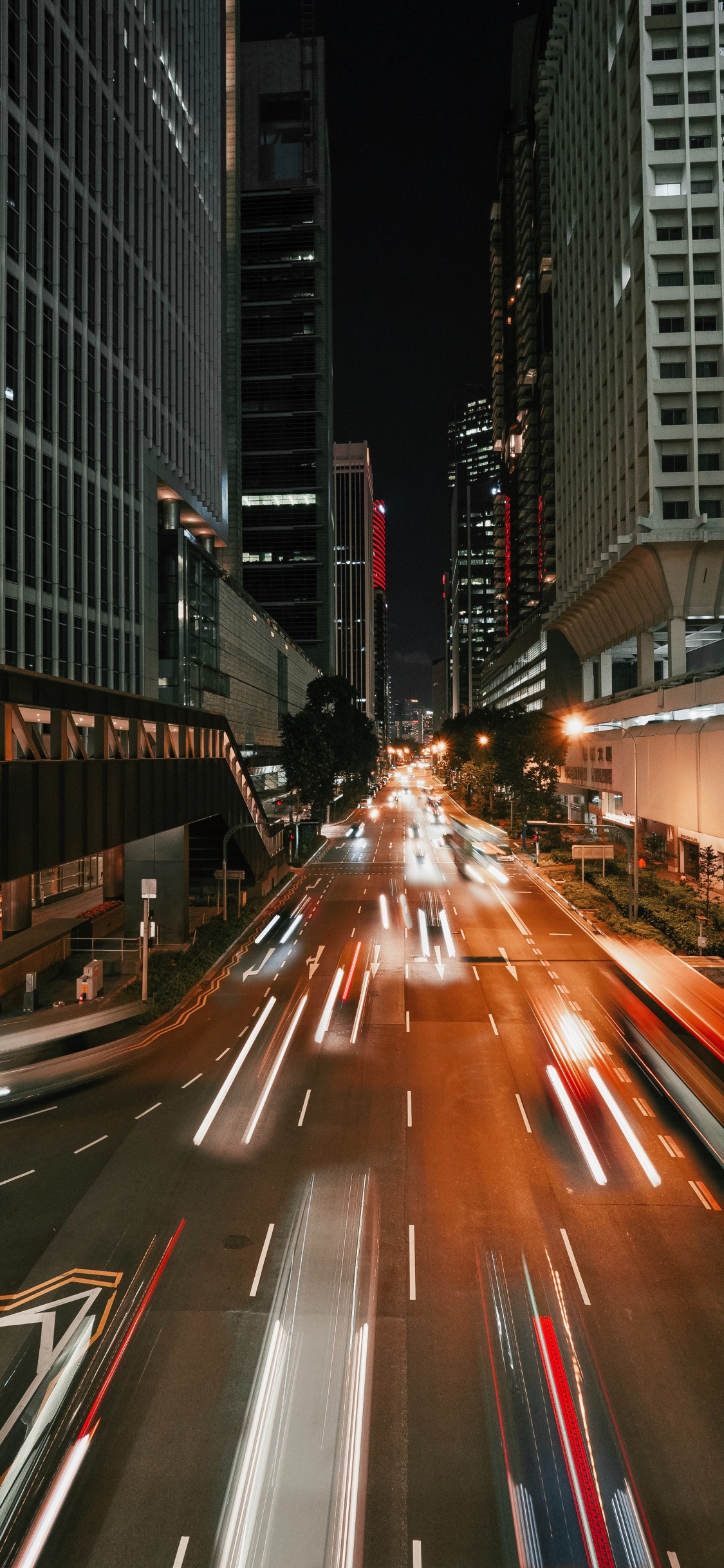Coches en la Carretera Entre Edificios de Gran Altura Durante la Noche. Wallpaper in 1125x2436 Resolution