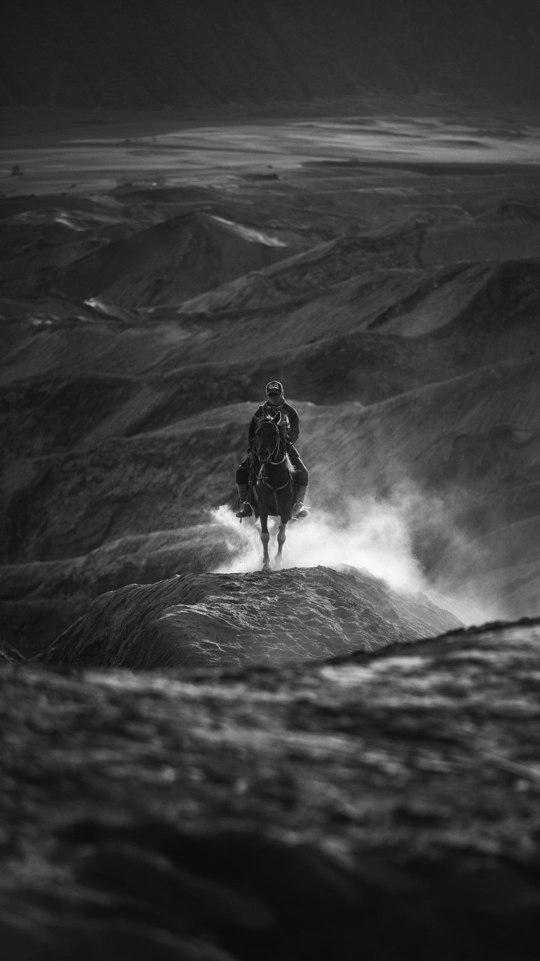 Grayscale Photo of Man in Black Jacket and Pants Standing on Rock Formation. Wallpaper in 1080x1920 Resolution