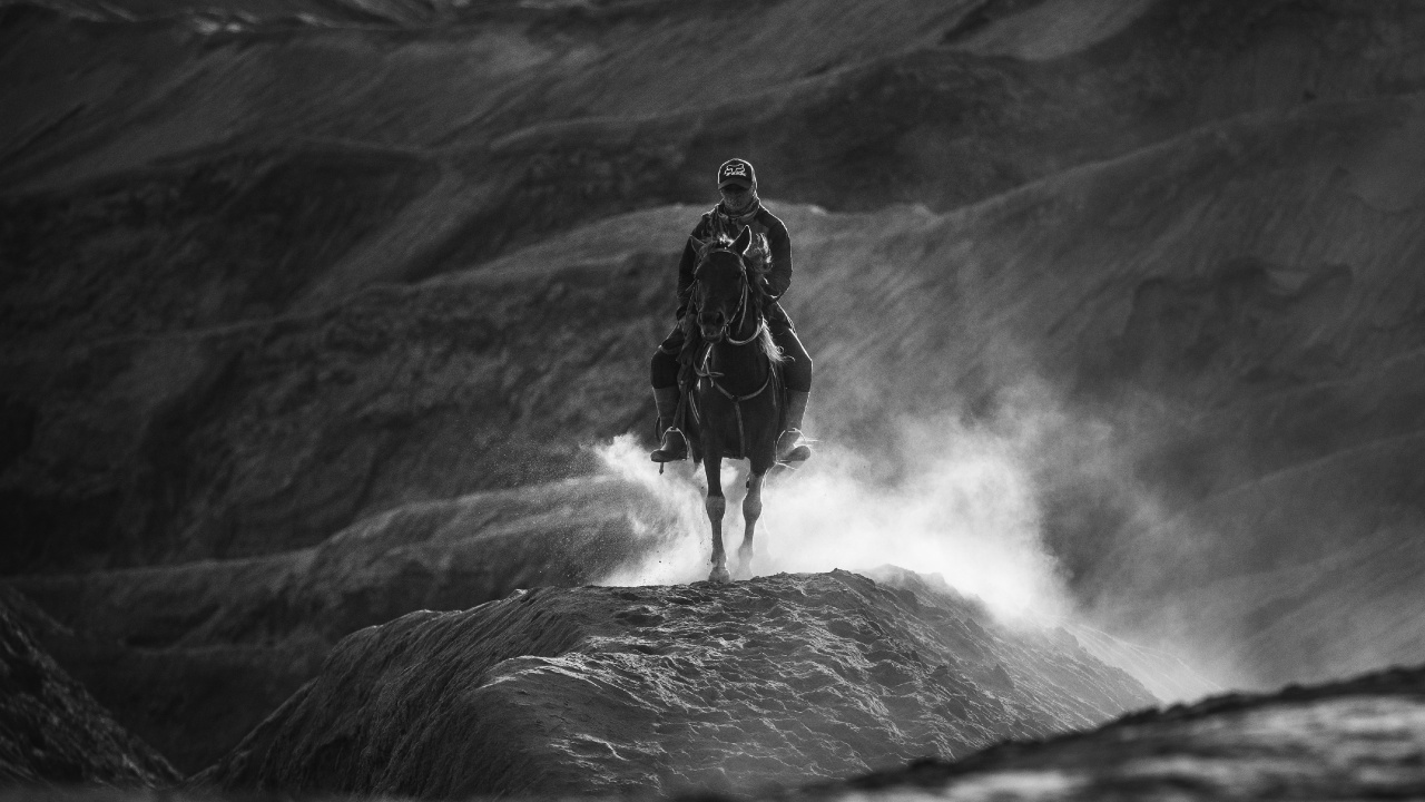 Grayscale Photo of Man in Black Jacket and Pants Standing on Rock Formation. Wallpaper in 1280x720 Resolution