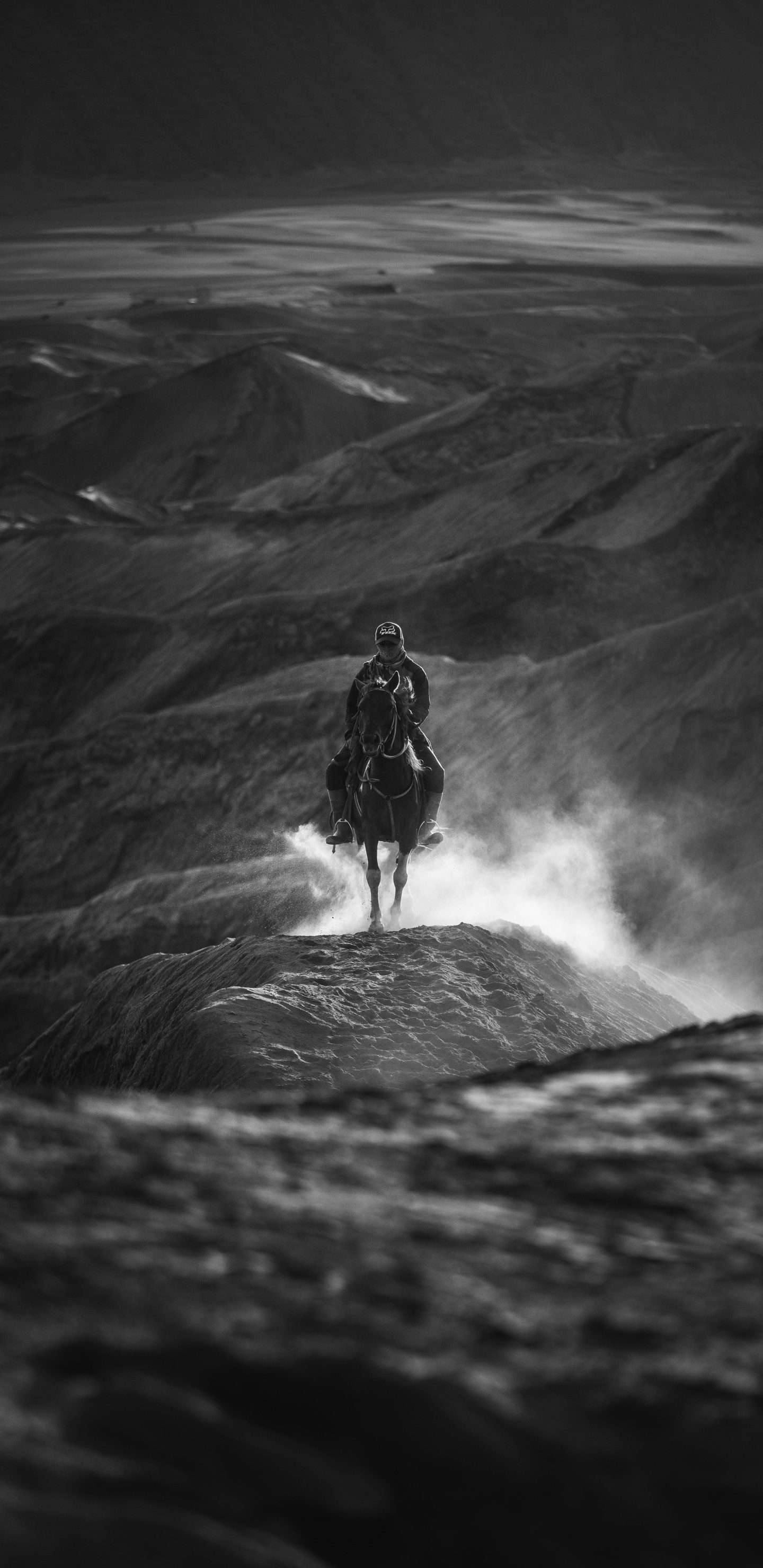 Grayscale Photo of Man in Black Jacket and Pants Standing on Rock Formation. Wallpaper in 1440x2960 Resolution