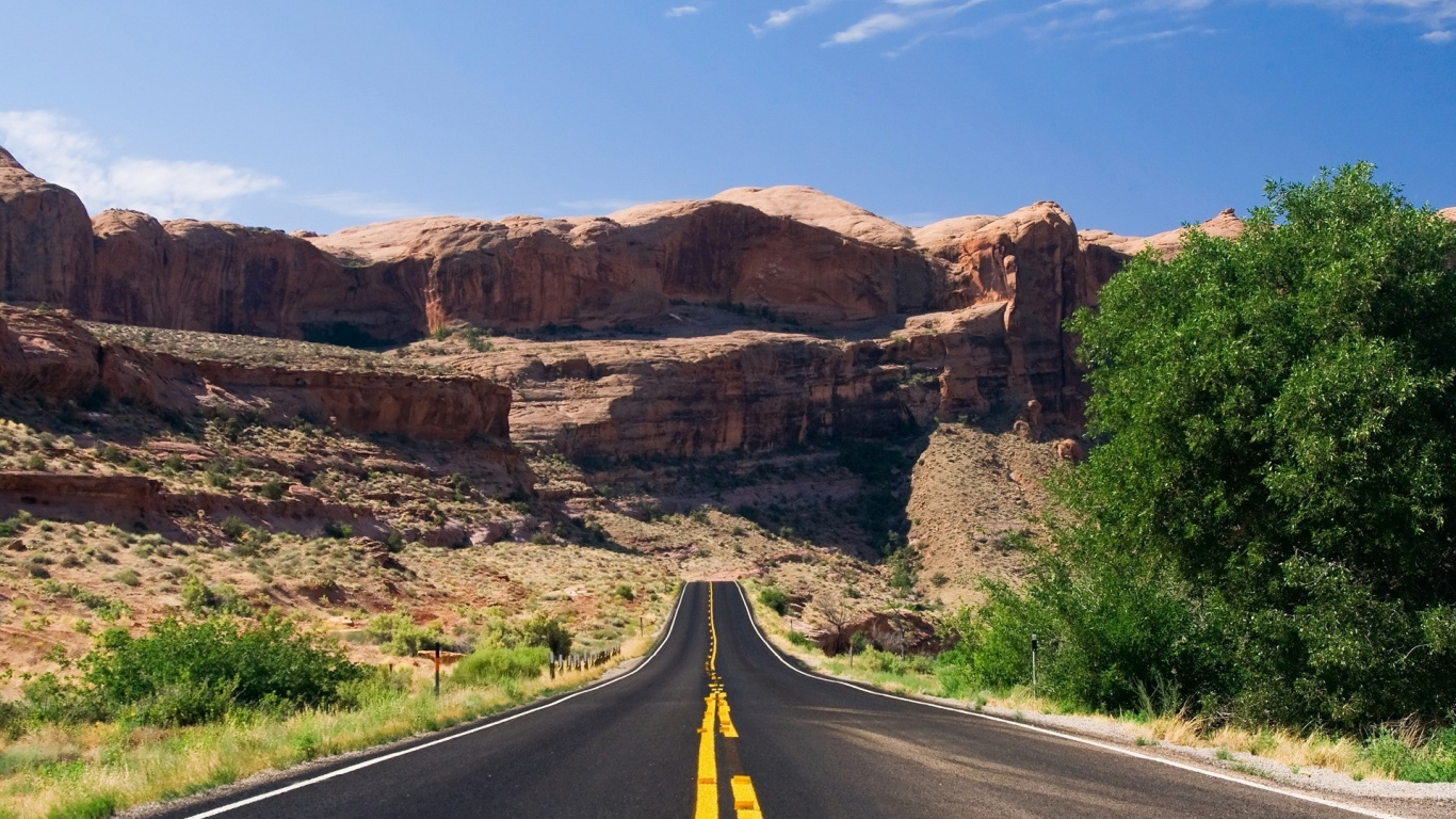 Gray Asphalt Road Between Brown Rock Formation Under Blue Sky During Daytime. Wallpaper in 1366x768 Resolution