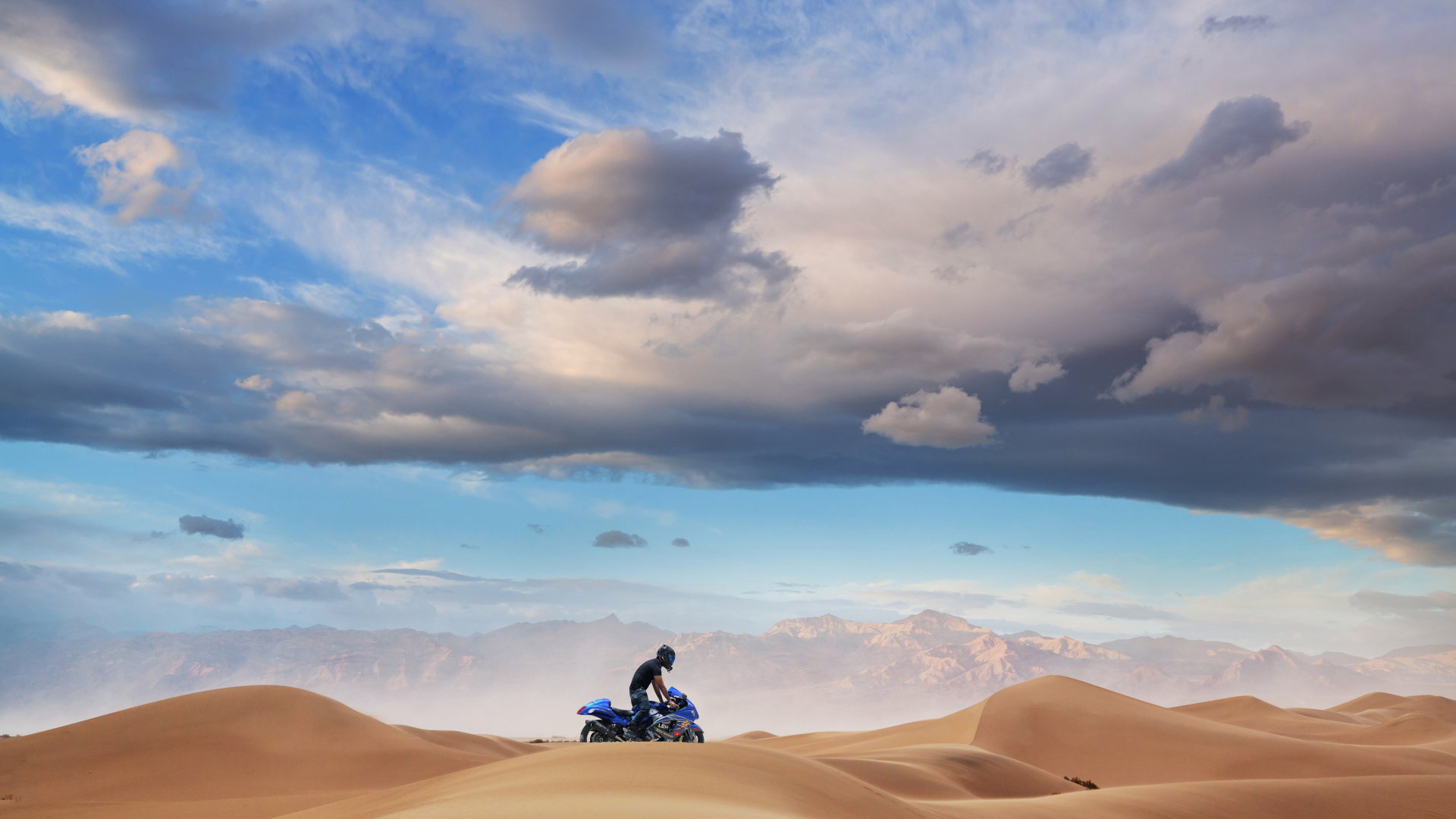 Man in Black Jacket and Black Pants Sitting on Brown Sand Under Blue Sky During Daytime. Wallpaper in 1920x1080 Resolution