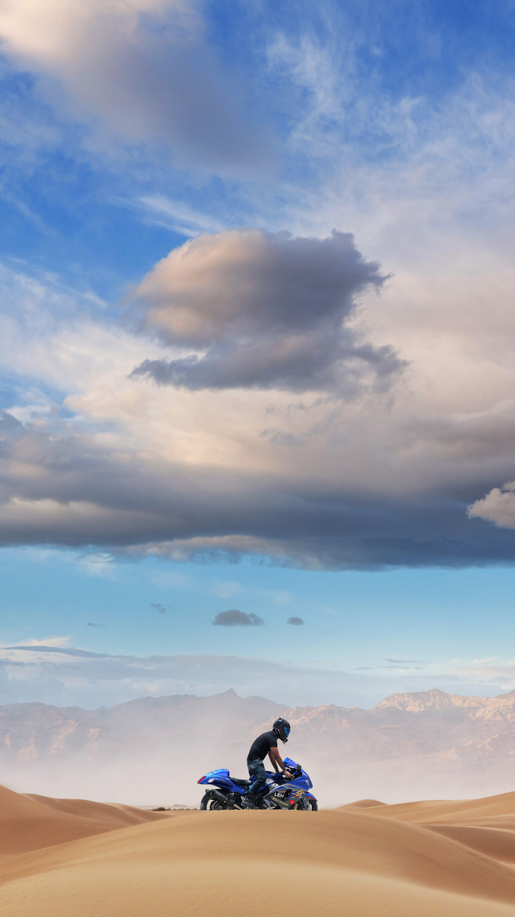 Man in Black Jacket and Black Pants Sitting on Brown Sand Under Blue Sky During Daytime. Wallpaper in 750x1334 Resolution