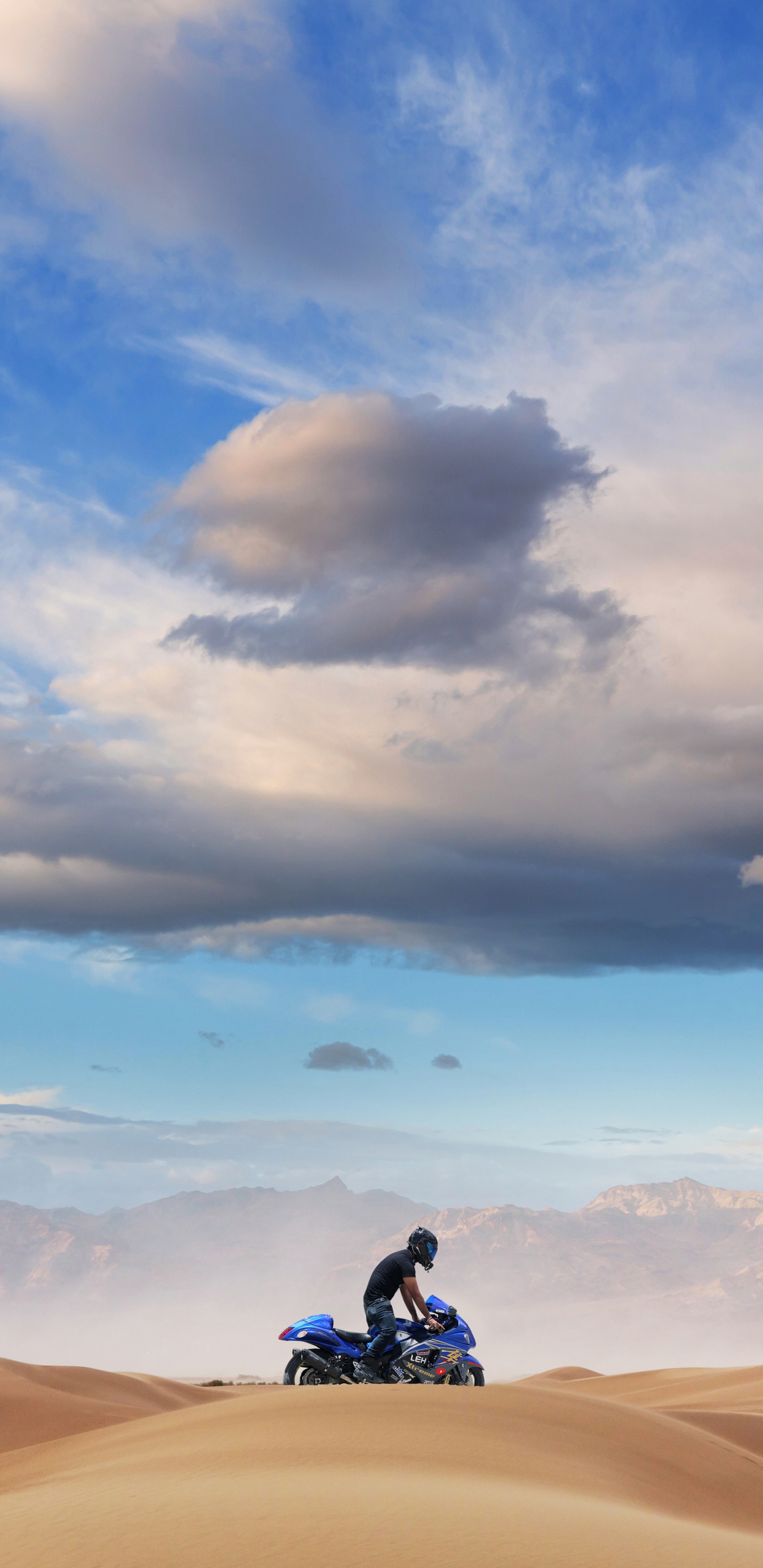 Mann in Schwarzer Jacke Und Schwarzer Hose, Der Tagsüber Auf Braunem Sand Unter Blauem Himmel Sitzt. Wallpaper in 1440x2960 Resolution