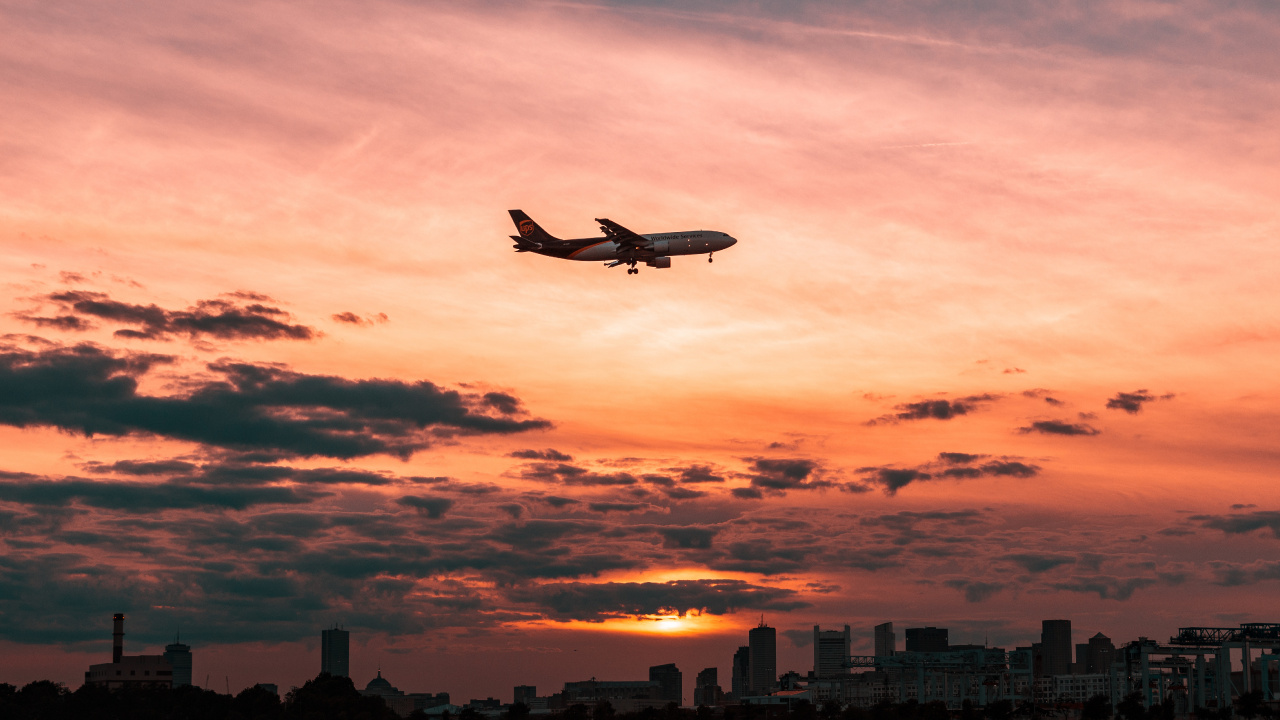 Weißes Flugzeug, Das Während Des Sonnenuntergangs Über Die Stadt Fliegt. Wallpaper in 1280x720 Resolution