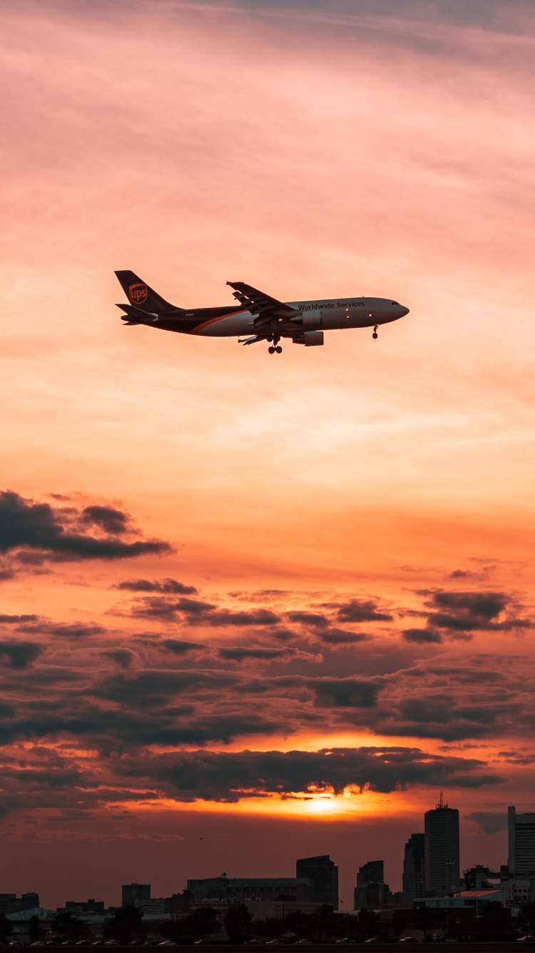 Weißes Flugzeug, Das Während Des Sonnenuntergangs Über Die Stadt Fliegt. Wallpaper in 750x1334 Resolution