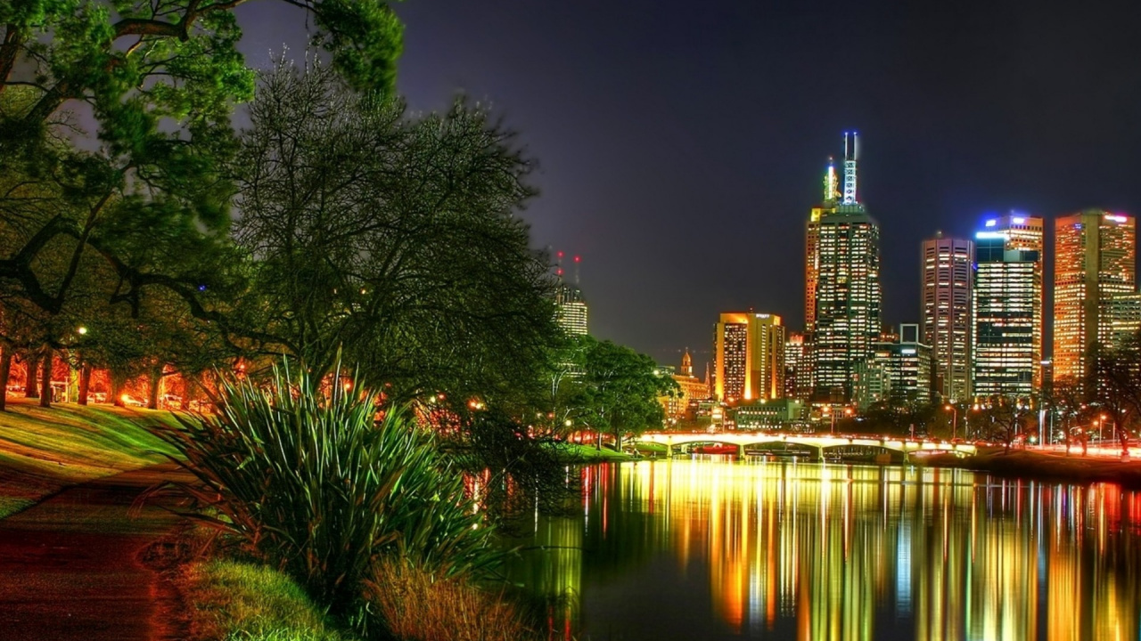 Body of Water Near Green Trees and High Rise Buildings During Night Time. Wallpaper in 1280x720 Resolution