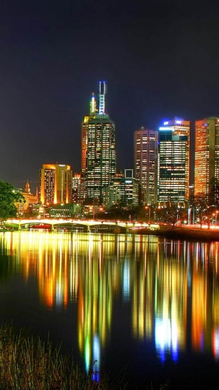 Body of Water Near Green Trees and High Rise Buildings During Night Time. Wallpaper in 750x1334 Resolution