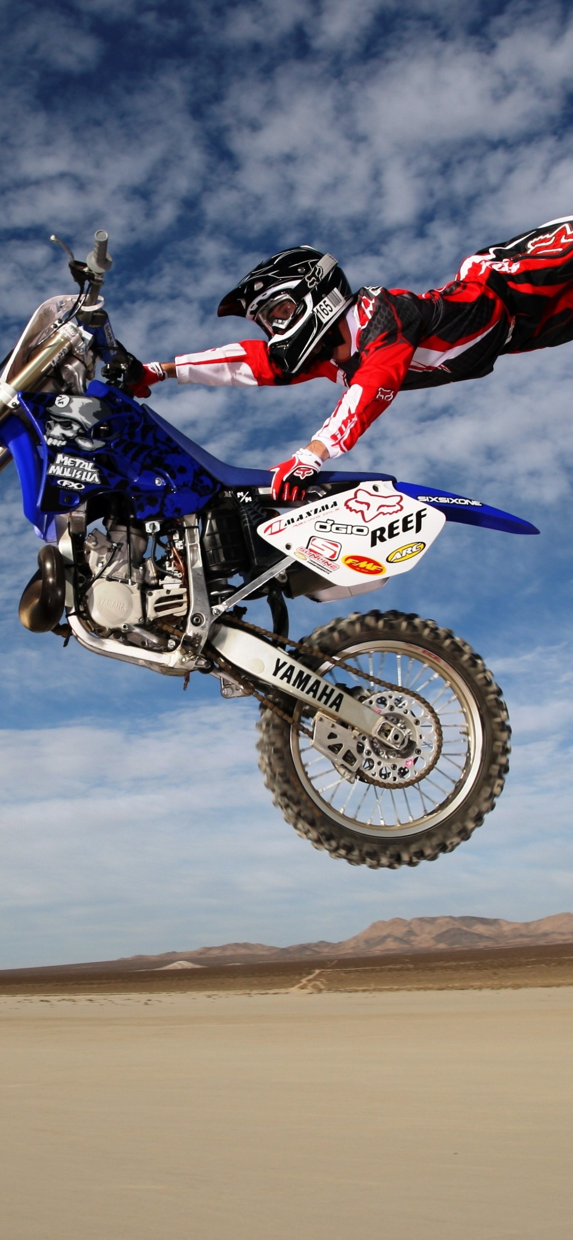 Mann, Der Tagsüber Motocross-Dirtbike Auf Braunem Sand Unter Blauem Himmel Fährt. Wallpaper in 1125x2436 Resolution