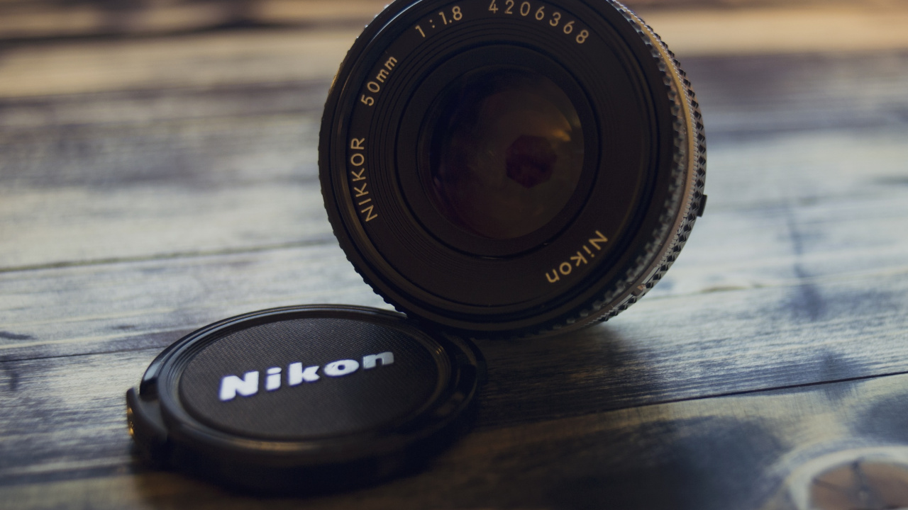 Schwarzes Nikon-Kameraobjektiv Auf Braunem Holztisch. Wallpaper in 1280x720 Resolution