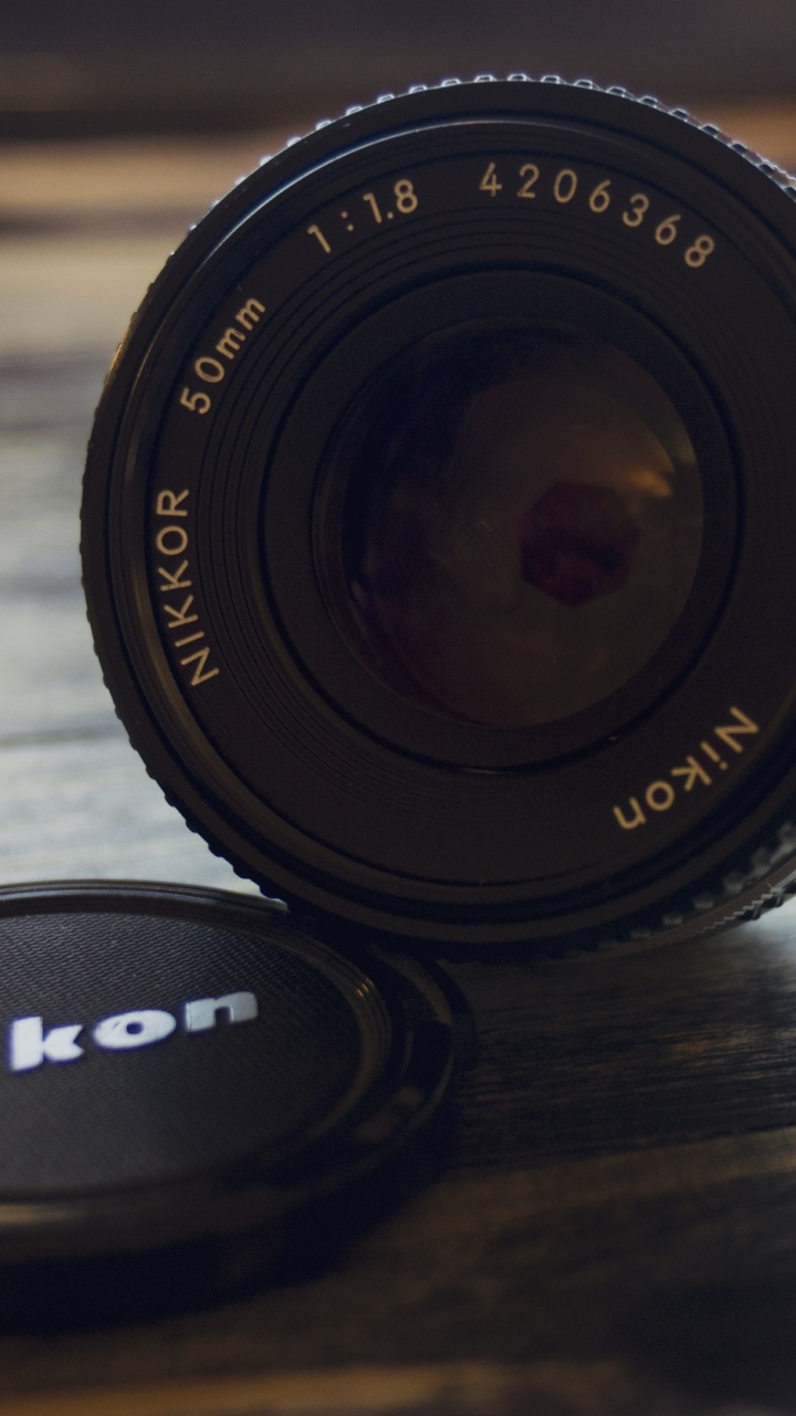 Schwarzes Nikon-Kameraobjektiv Auf Braunem Holztisch. Wallpaper in 720x1280 Resolution