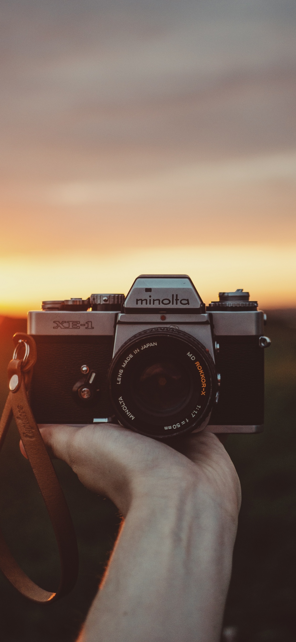 Person, Die Während Des Sonnenuntergangs Eine Schwarze Und Silberne Nikon-Dslr-Kamera Hält. Wallpaper in 1242x2688 Resolution
