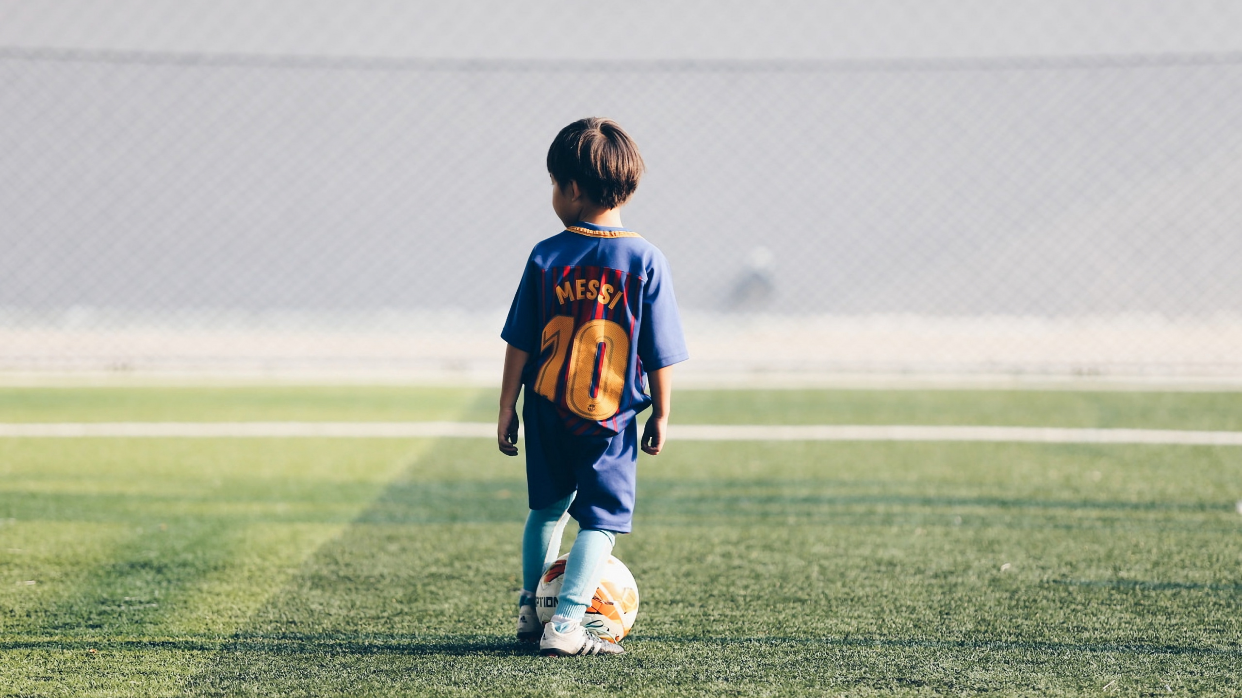 Niño Con Camiseta de Fútbol Azul y Roja y Pantalones Cortos Blancos Corriendo en el Campo de Hierba Verde. Wallpaper in 2560x1440 Resolution