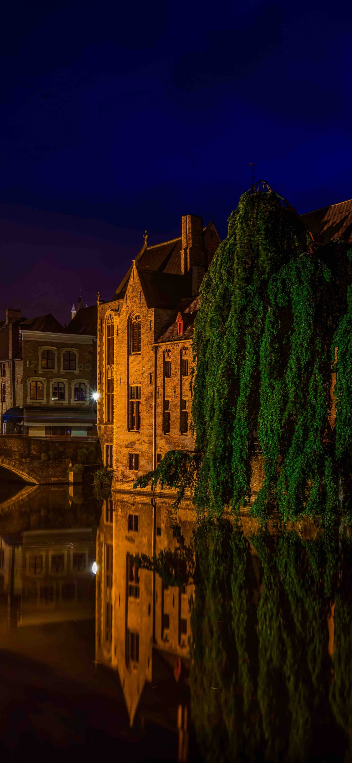 Bâtiment en Béton Brun Près D'un Plan D'eau Pendant la Nuit. Wallpaper in 1125x2436 Resolution