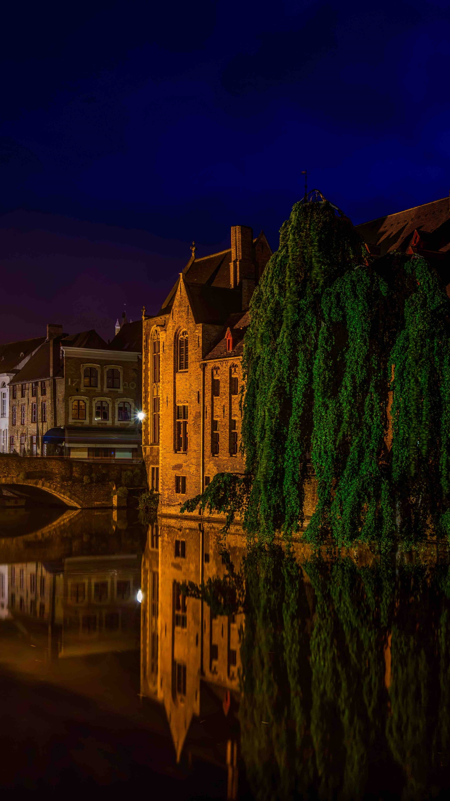 Brown Concrete Building Near Body of Water During Night Time. Wallpaper in 1440x2560 Resolution
