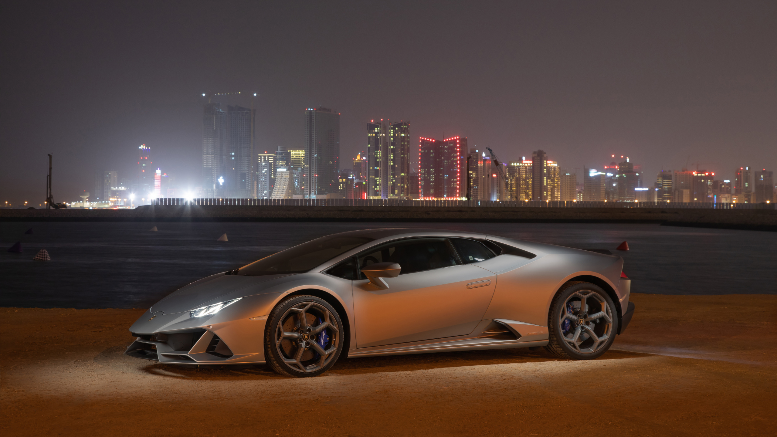 Coupe Blanco Estacionado en el Campo Marrón Cerca de Los Edificios de la Ciudad Durante la Noche. Wallpaper in 2560x1440 Resolution