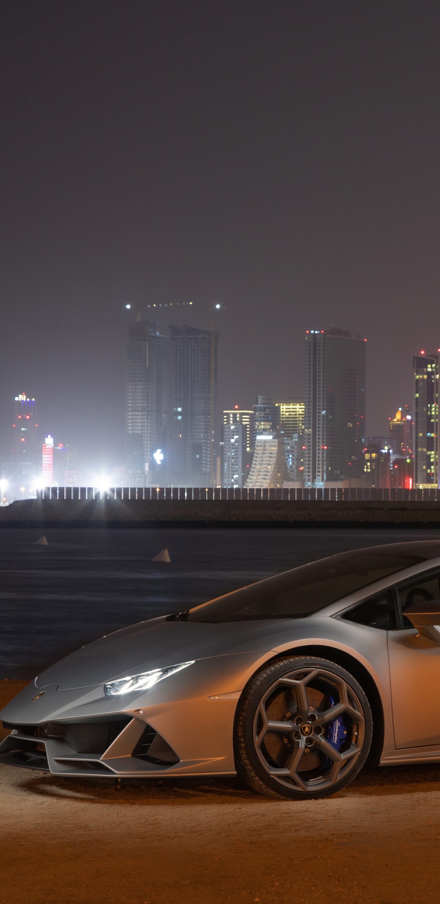 White Coupe Parked on Brown Field Near City Buildings During Night Time. Wallpaper in 1440x2960 Resolution