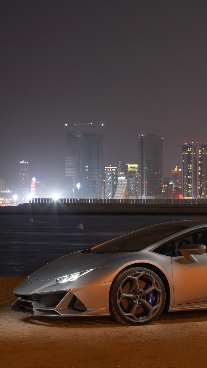 White Coupe Parked on Brown Field Near City Buildings During Night Time. Wallpaper in 720x1280 Resolution