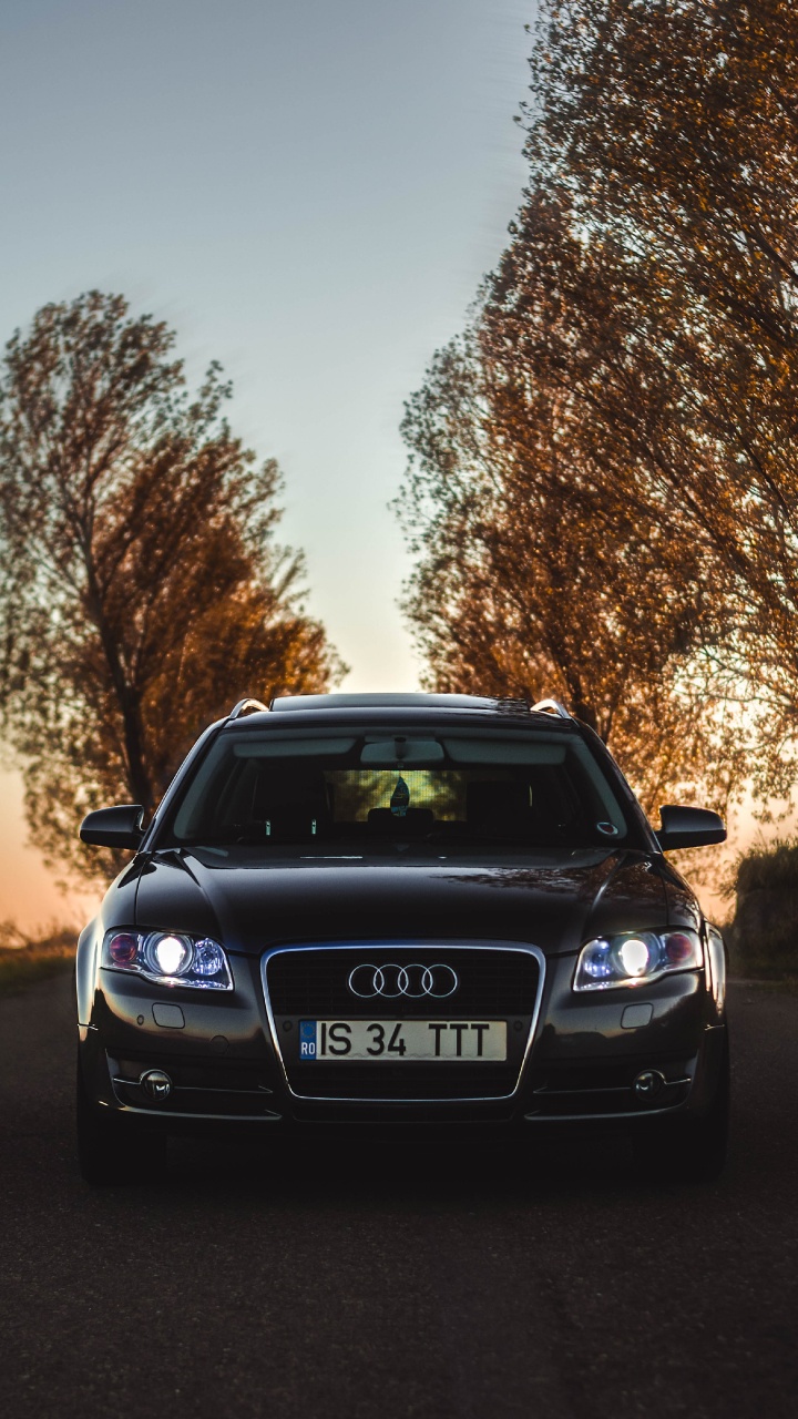 Schwarzer Audi a 4 Parkte Bei Sonnenuntergang Auf Grüner Wiese. Wallpaper in 720x1280 Resolution