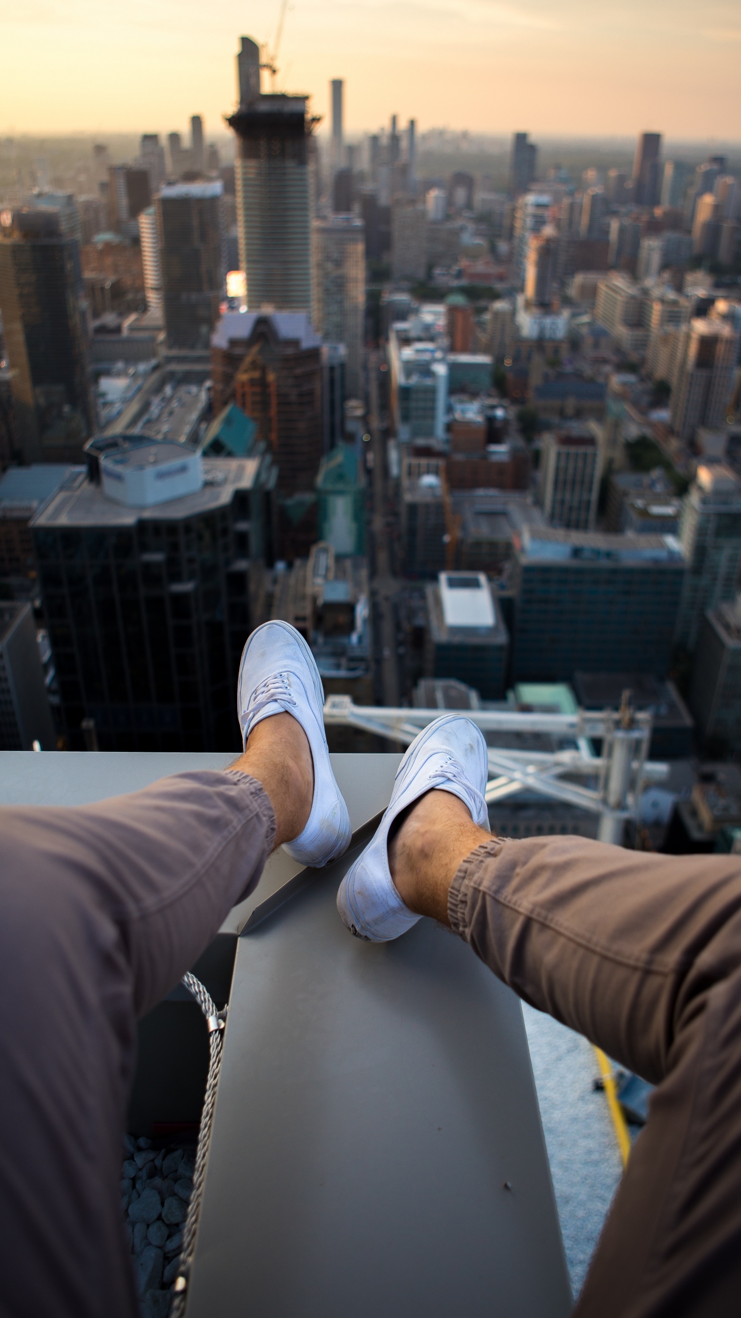 Person in Brown Pants and White Sneakers Sitting on White Building During Daytime. Wallpaper in 1440x2560 Resolution