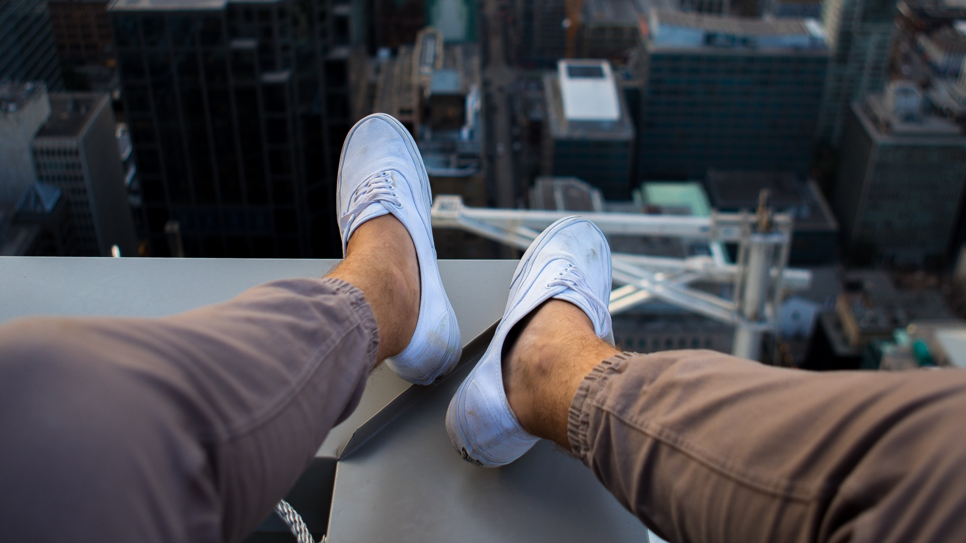 Person in Brown Pants and White Sneakers Sitting on White Building During Daytime. Wallpaper in 1920x1080 Resolution