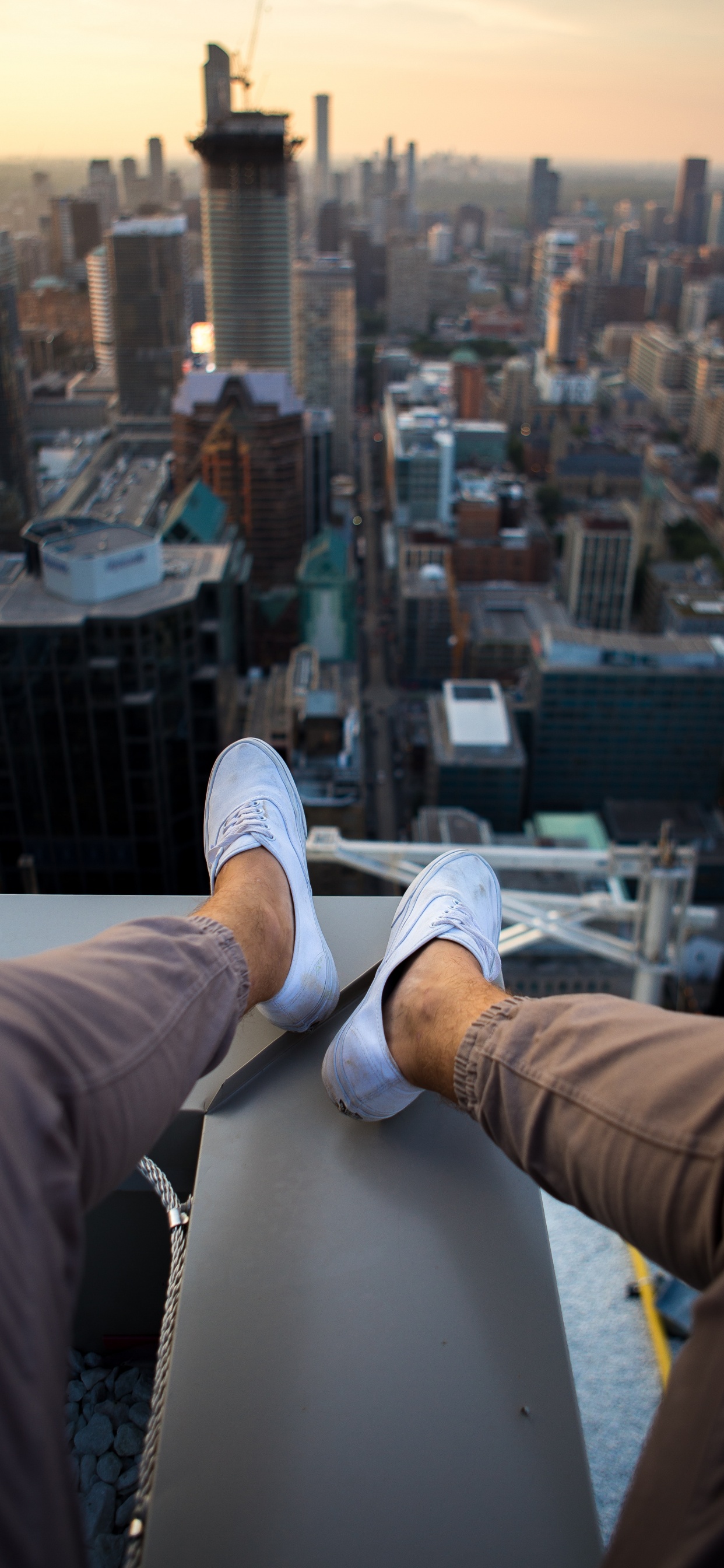 Personne en Pantalon Marron et Baskets Blanches Assis Sur un Bâtiment Blanc Pendant la Journée. Wallpaper in 1242x2688 Resolution