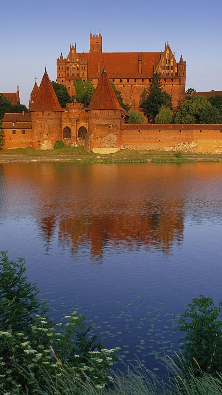 Brown Concrete Building Near Green Grass and Body of Water During Daytime. Wallpaper in 750x1334 Resolution