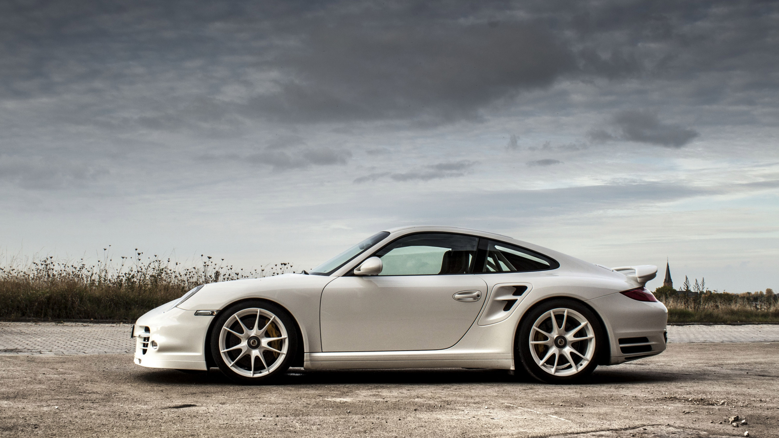 White Porsche 911 on Gray Asphalt Road Under Gray Cloudy Sky. Wallpaper in 2560x1440 Resolution