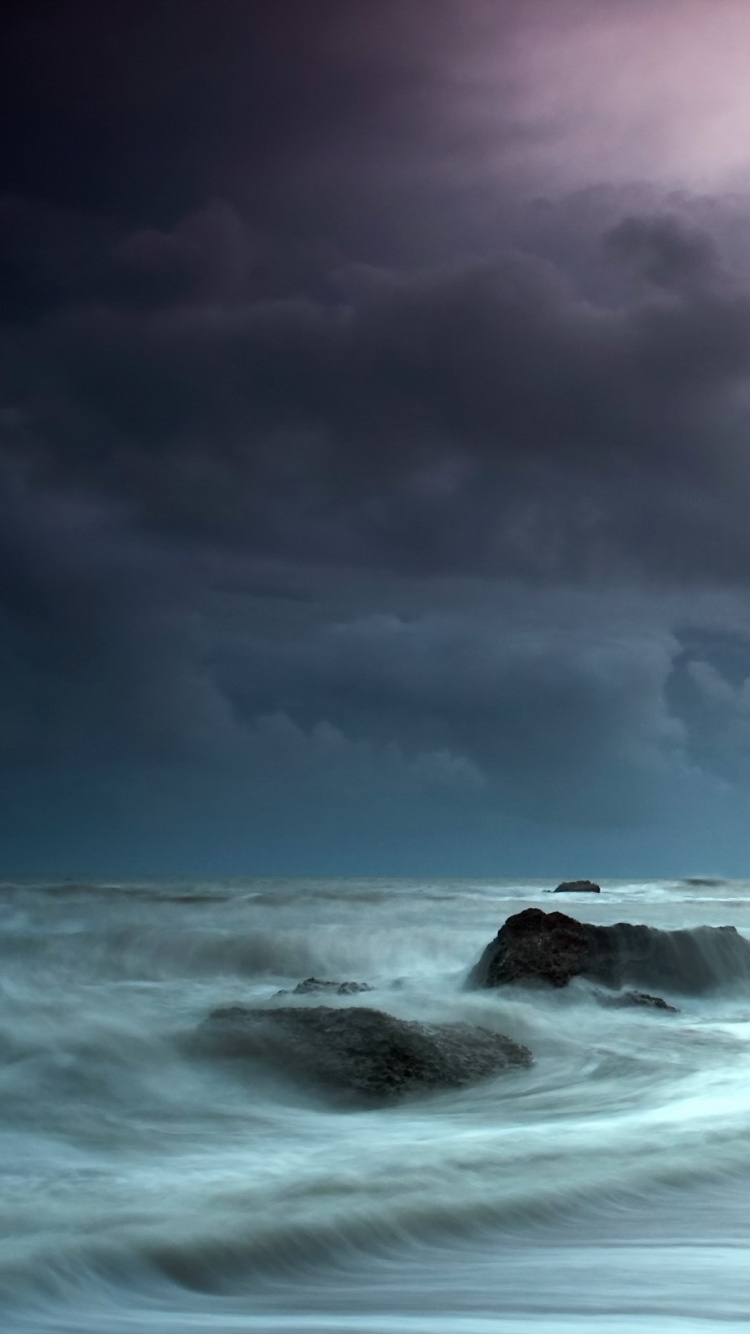 Olas Del Océano Rompiendo Contra Las Rocas Bajo el Cielo Nublado. Wallpaper in 750x1334 Resolution